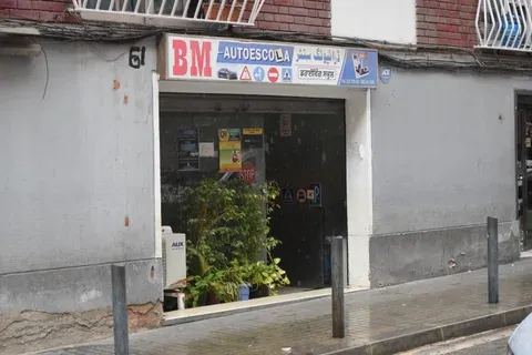 The BM Autoescola shopfront in Badalona. The sign reads "BM AUTOESCOLA" in Spanish, "ڈرائیونگ سنٹر" in Urdu and "ਡਰਾਈਵਿੰਗ ਸਕੂਲ" in Punjabi, above a row of Spanish road signs.